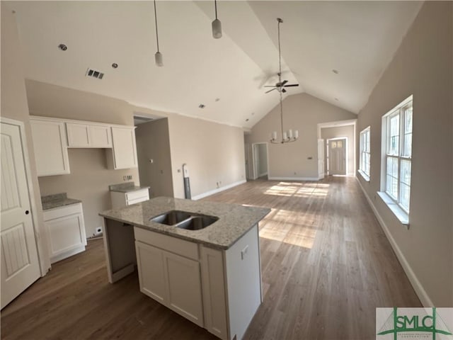 kitchen with white cabinetry, light stone counters, dark hardwood / wood-style flooring, a center island with sink, and ceiling fan with notable chandelier