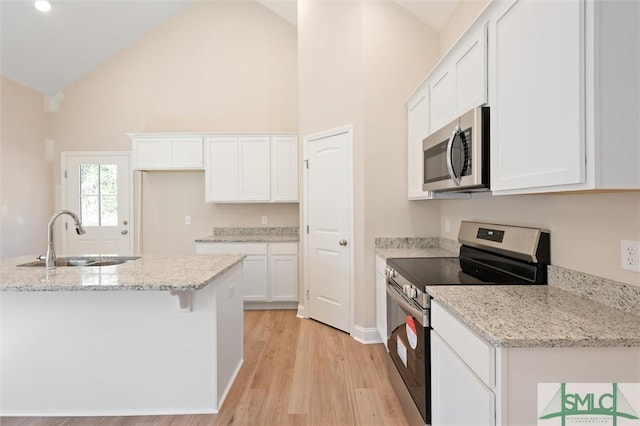 kitchen with light stone counters, light wood finished floors, appliances with stainless steel finishes, white cabinets, and a sink