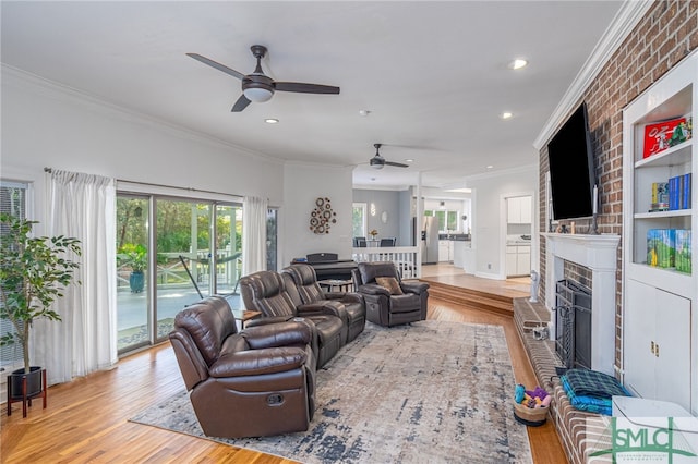 living room featuring a fireplace, ceiling fan, light hardwood / wood-style flooring, and crown molding