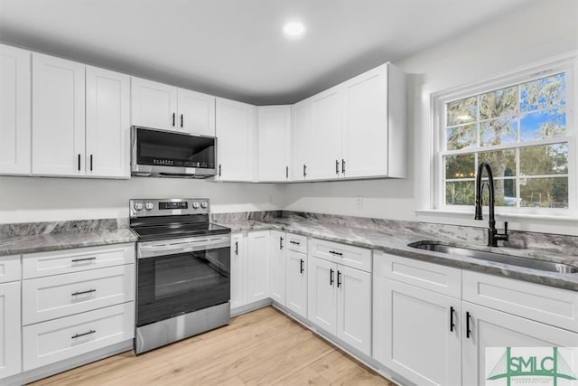 kitchen with stainless steel appliances, light hardwood / wood-style floors, dark stone counters, white cabinets, and sink