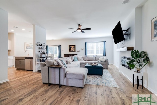 living room with ceiling fan, sink, a fireplace, and light wood-type flooring