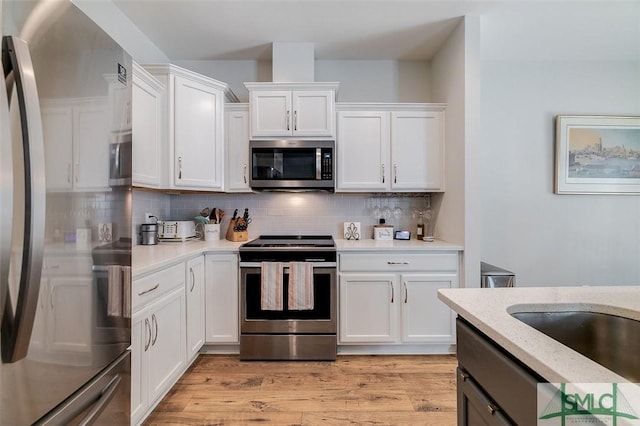 kitchen featuring appliances with stainless steel finishes, tasteful backsplash, light stone counters, light hardwood / wood-style floors, and white cabinets