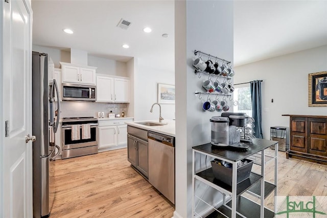 kitchen with tasteful backsplash, white cabinetry, sink, stainless steel appliances, and light wood-type flooring