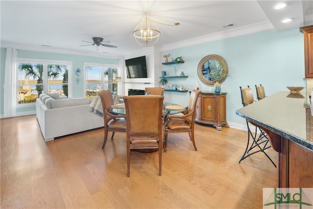 dining space with ceiling fan with notable chandelier, a large fireplace, crown molding, and light hardwood / wood-style flooring