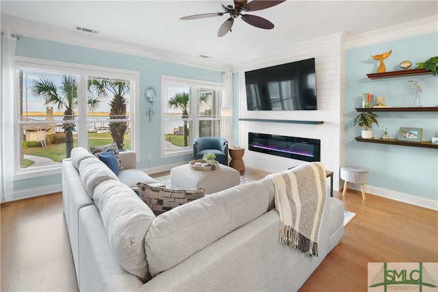 living room featuring light wood-type flooring, a large fireplace, ceiling fan, and ornamental molding