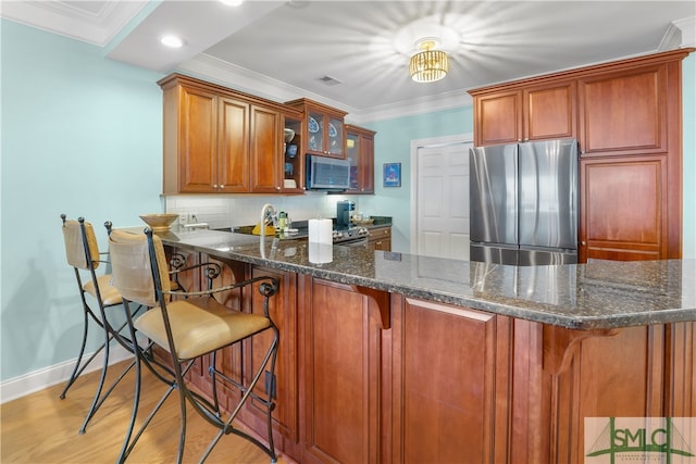 kitchen featuring dark stone counters, ornamental molding, a kitchen bar, kitchen peninsula, and stainless steel appliances