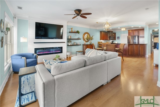 living room with a healthy amount of sunlight, light hardwood / wood-style flooring, crown molding, a fireplace, and ceiling fan with notable chandelier