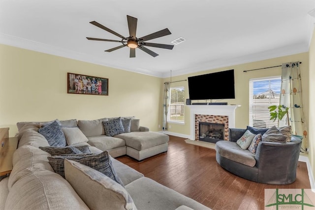 living room featuring ceiling fan, a tiled fireplace, crown molding, and dark hardwood / wood-style flooring