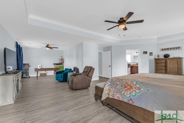 bedroom featuring ceiling fan, ensuite bath, light hardwood / wood-style flooring, and a tray ceiling