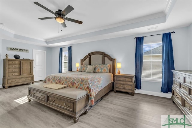 bedroom featuring ceiling fan, ornamental molding, light wood-type flooring, and a tray ceiling