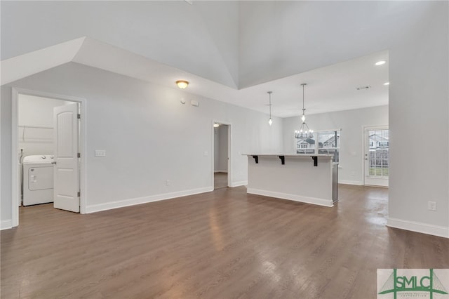 unfurnished living room with washer / clothes dryer, lofted ceiling, an inviting chandelier, and dark hardwood / wood-style floors