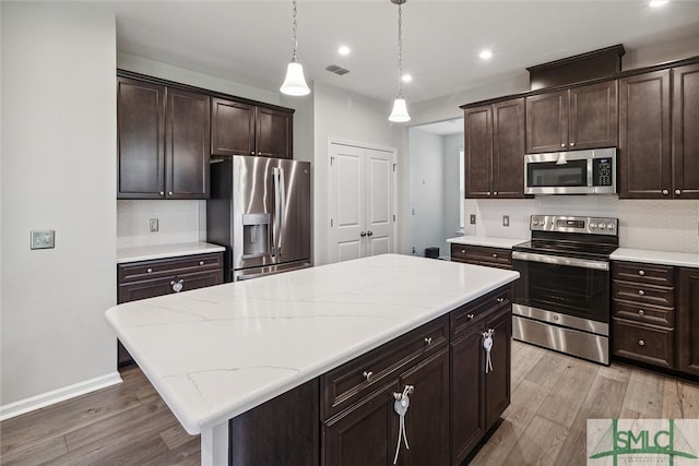 kitchen featuring appliances with stainless steel finishes, tasteful backsplash, pendant lighting, a center island, and light hardwood / wood-style floors