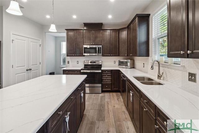 kitchen with sink, hanging light fixtures, appliances with stainless steel finishes, light wood-type flooring, and light stone counters