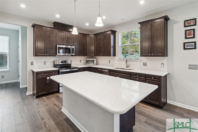 kitchen featuring hanging light fixtures, a kitchen island, stainless steel appliances, and light wood-type flooring