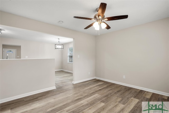 spare room featuring ceiling fan with notable chandelier and wood-type flooring