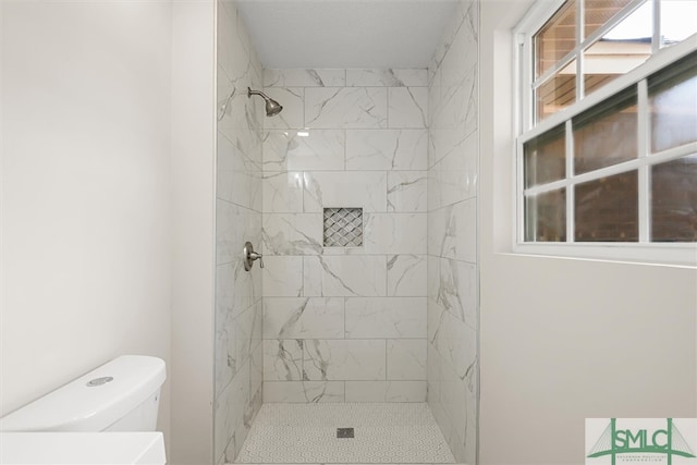 bathroom featuring toilet, tiled shower, and a healthy amount of sunlight