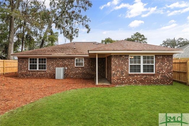 rear view of house with central air condition unit and a lawn