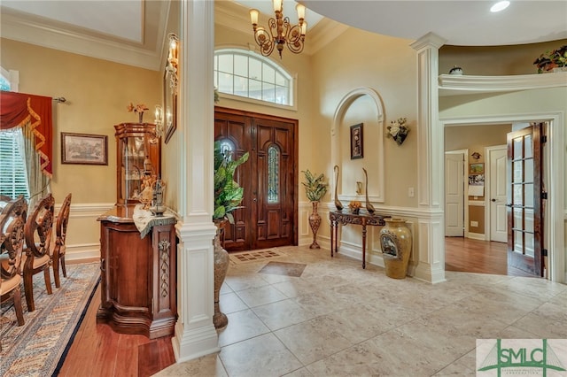 foyer entrance featuring a high ceiling, crown molding, decorative columns, and an inviting chandelier