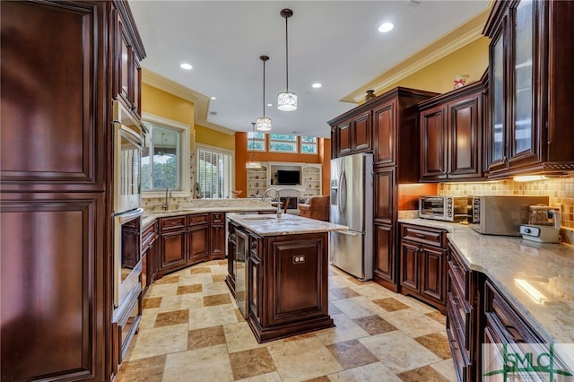 kitchen with a center island with sink, hanging light fixtures, appliances with stainless steel finishes, and crown molding