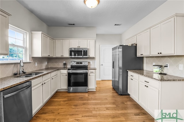 kitchen featuring sink, dark stone countertops, light wood-type flooring, white cabinetry, and stainless steel appliances