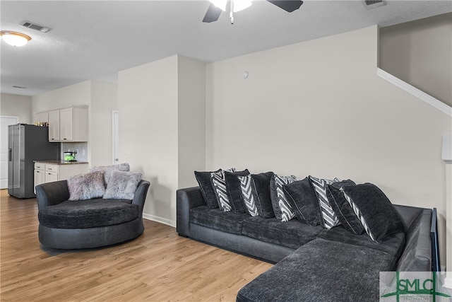 living room featuring a textured ceiling, light wood-type flooring, and ceiling fan