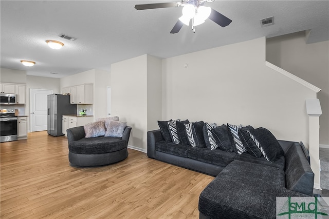 living room with a textured ceiling, light hardwood / wood-style flooring, and ceiling fan