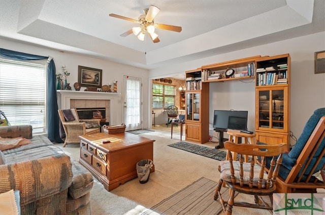 living room with a tile fireplace, light carpet, a tray ceiling, and ceiling fan