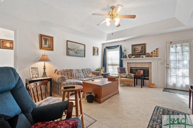 carpeted living room featuring a tile fireplace, a textured ceiling, a raised ceiling, and ceiling fan