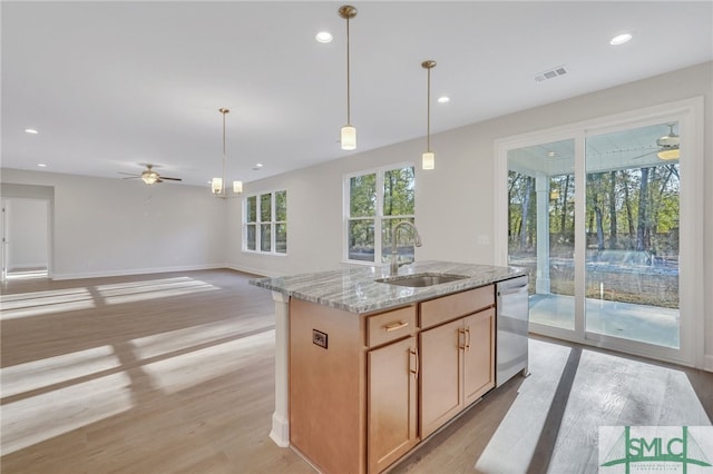 kitchen featuring dishwasher, a center island with sink, sink, light hardwood / wood-style flooring, and light stone countertops