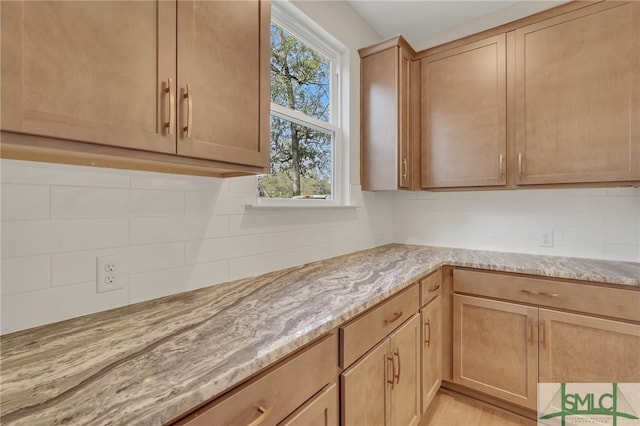 kitchen with backsplash, light stone counters, light brown cabinets, and light hardwood / wood-style floors