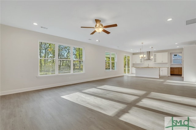 unfurnished living room featuring ceiling fan with notable chandelier and light wood-type flooring