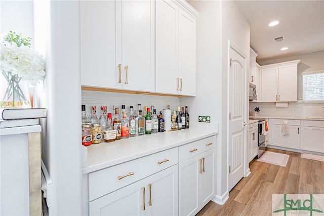 bar featuring white cabinets, stainless steel appliances, and light hardwood / wood-style floors