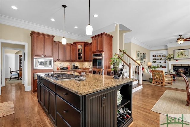 kitchen with pendant lighting, stainless steel appliances, ornamental molding, light hardwood / wood-style floors, and a kitchen island