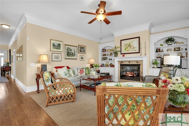 living room featuring built in shelves, hardwood / wood-style flooring, ceiling fan, and ornamental molding