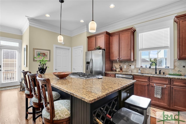 kitchen featuring sink, appliances with stainless steel finishes, light stone countertops, a kitchen island, and decorative light fixtures