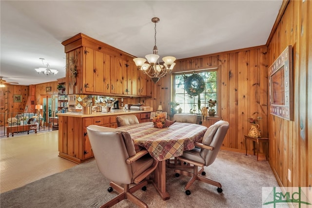 carpeted dining room featuring ceiling fan with notable chandelier, wood walls, and ornamental molding