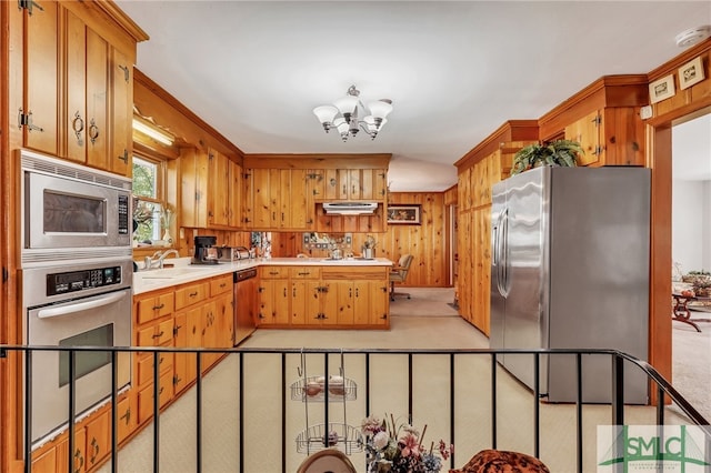 kitchen with ventilation hood, stainless steel appliances, light colored carpet, a chandelier, and wood walls