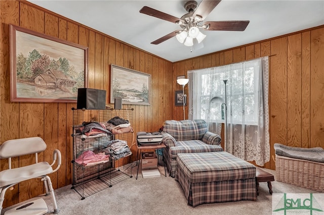 sitting room with wood walls, ceiling fan, and light carpet