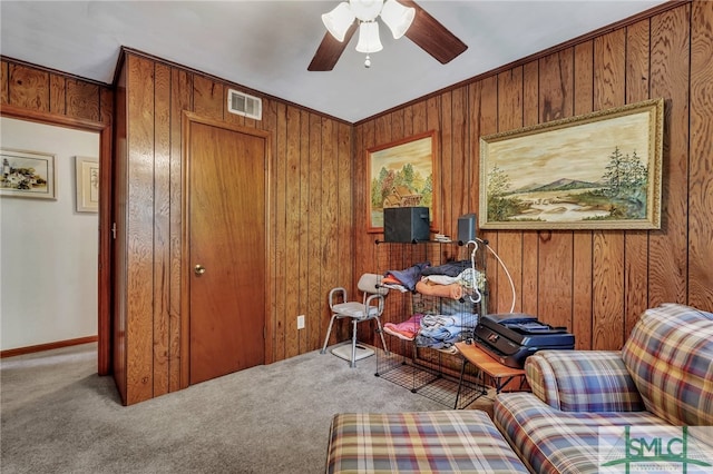 sitting room featuring ceiling fan, carpet floors, crown molding, and wooden walls