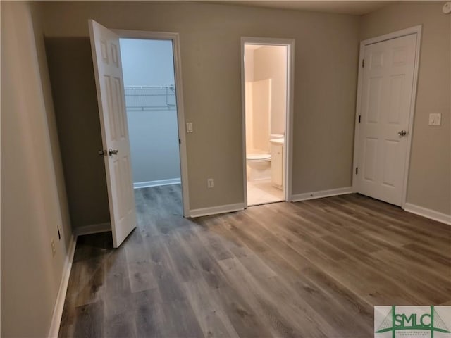 unfurnished bedroom featuring a spacious closet, baseboards, and wood finished floors