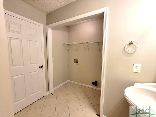 laundry area featuring baseboards, hookup for a washing machine, a textured ceiling, a sink, and light tile patterned flooring