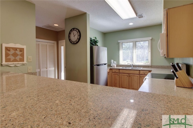 kitchen with stainless steel refrigerator, sink, light stone counters, a textured ceiling, and range