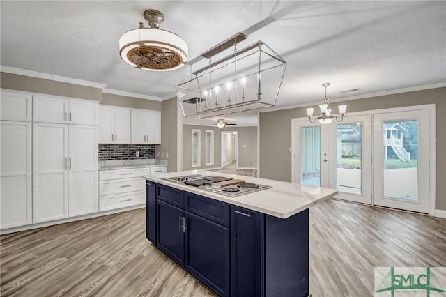 kitchen featuring a kitchen island, stainless steel gas stovetop, blue cabinets, white cabinets, and hanging light fixtures