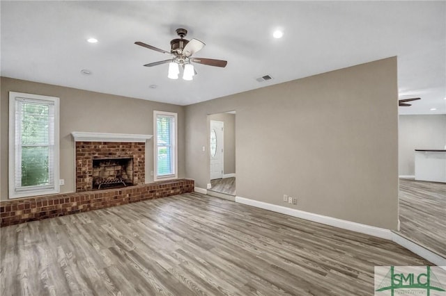 unfurnished living room featuring ceiling fan, a brick fireplace, and light wood-type flooring