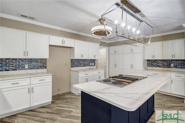 kitchen featuring a kitchen island, decorative light fixtures, stainless steel gas stovetop, white cabinetry, and ornamental molding