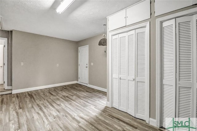 unfurnished bedroom with two closets, light hardwood / wood-style flooring, and a textured ceiling