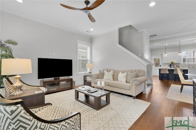 living room with dark hardwood / wood-style flooring, ceiling fan, and ornamental molding