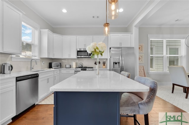 kitchen with pendant lighting, a center island, appliances with stainless steel finishes, and light hardwood / wood-style flooring