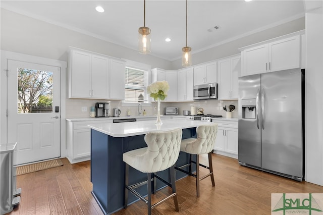 kitchen with white cabinets, light hardwood / wood-style floors, hanging light fixtures, and appliances with stainless steel finishes