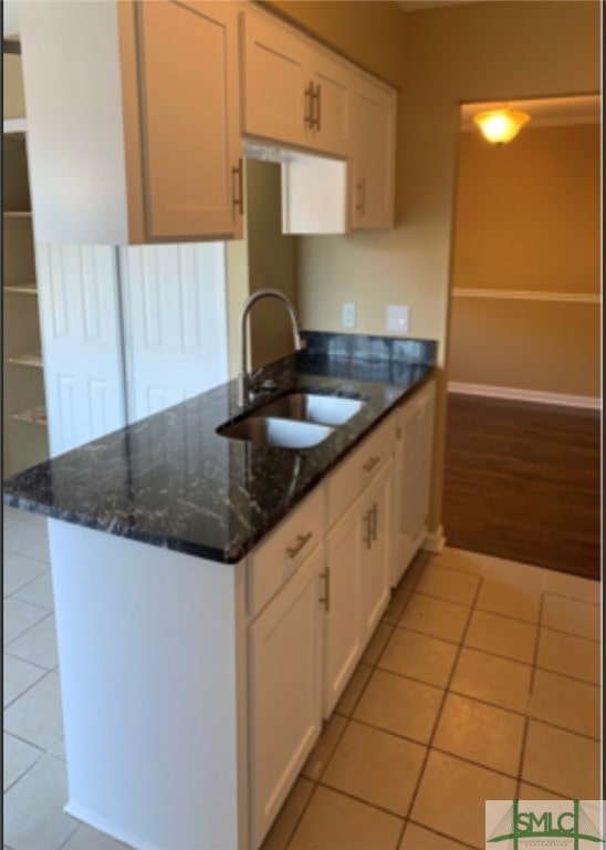 kitchen featuring dark stone counters, white cabinets, sink, light tile patterned floors, and kitchen peninsula